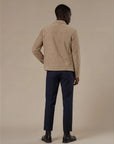 Back view of man wearing a beige suede jacket and dark formal pants with black chelsea boots