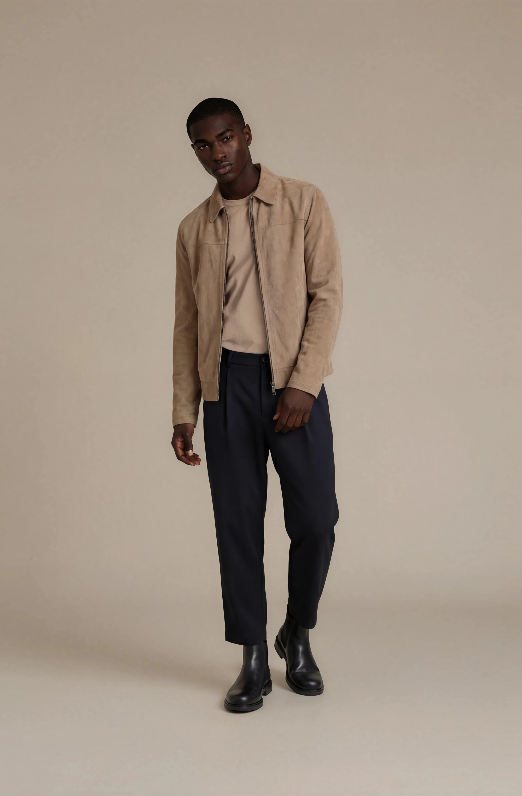 Man wearing a beige suede jacket, beige shirt and dark formal pants with black chelsea boots