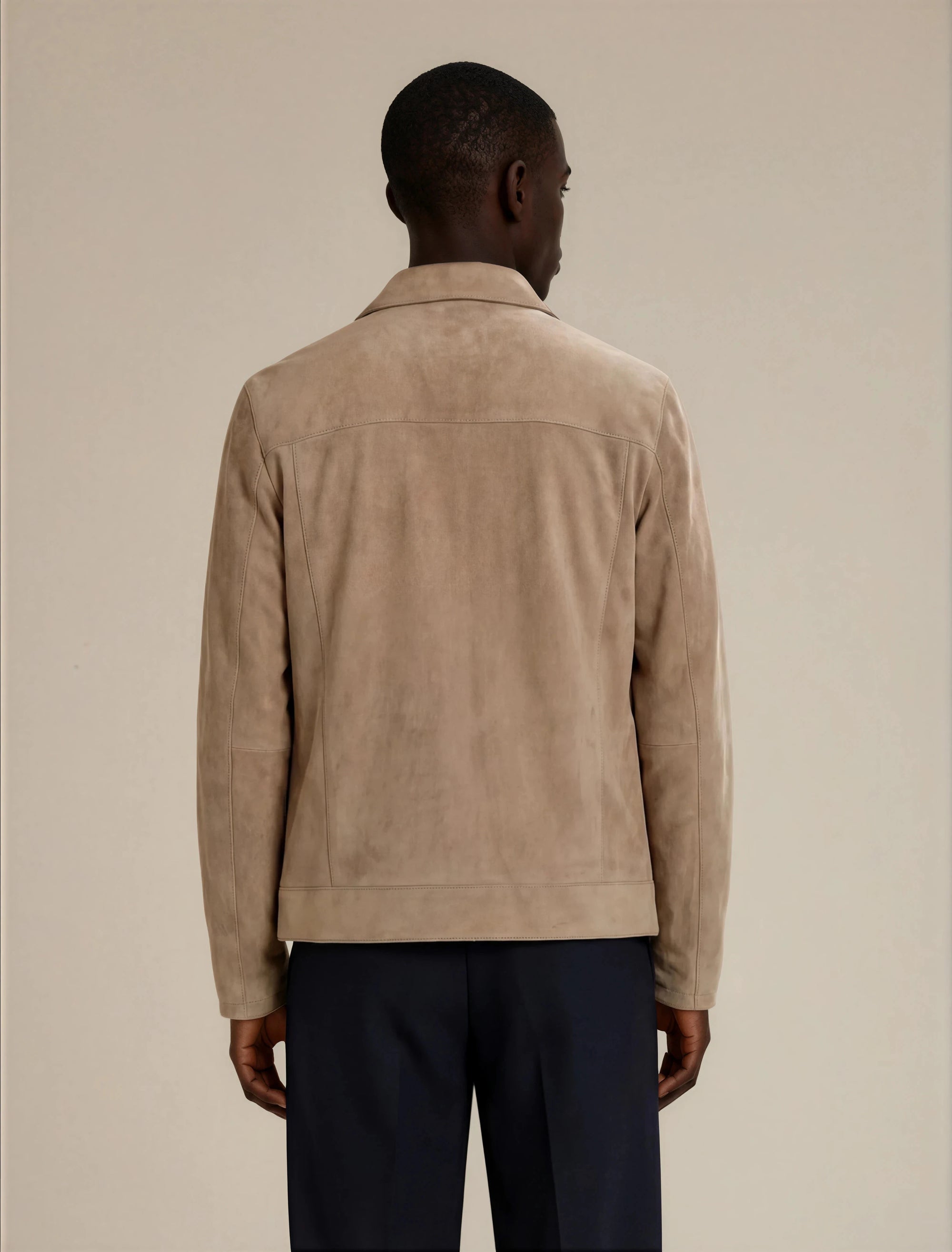 Back view of a man wearing a beige suede jacket and dark formal pants