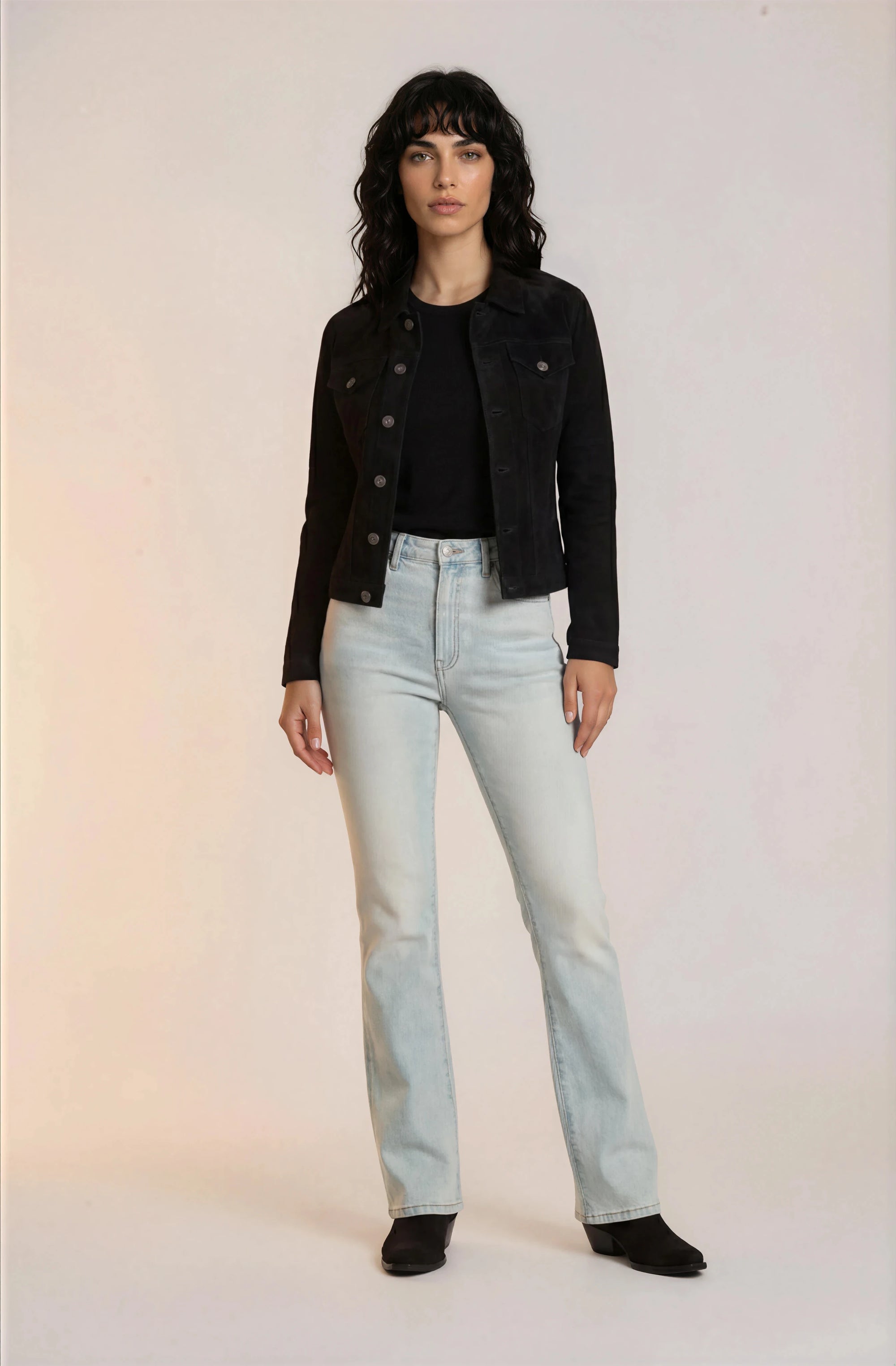 Woman wearing a black jacket, black top, and light blue jeans on a white background