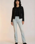 Woman wearing a black jacket, black top, and light blue jeans on a white background
